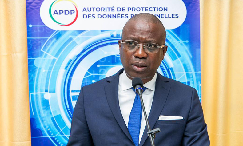Homme en costume bleu et cravate parlant devant un micro avec un panneau de l’Autorité de protection des données en arrière-plan
