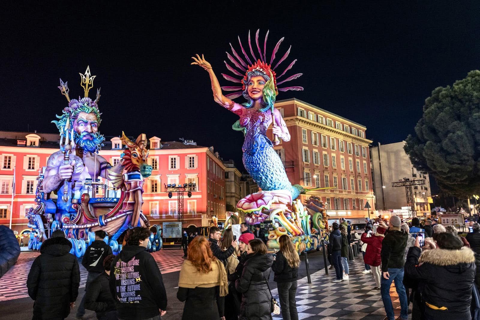 Deux grandes sculptures colorées de figures marines illuminées entourées de spectateurs en extérieur la nuit