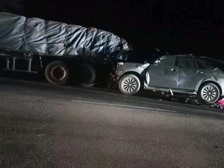 Une voiture SUV endommagée est encastrée à l'avant dans un poids lourd arrêté sur une route de nuit