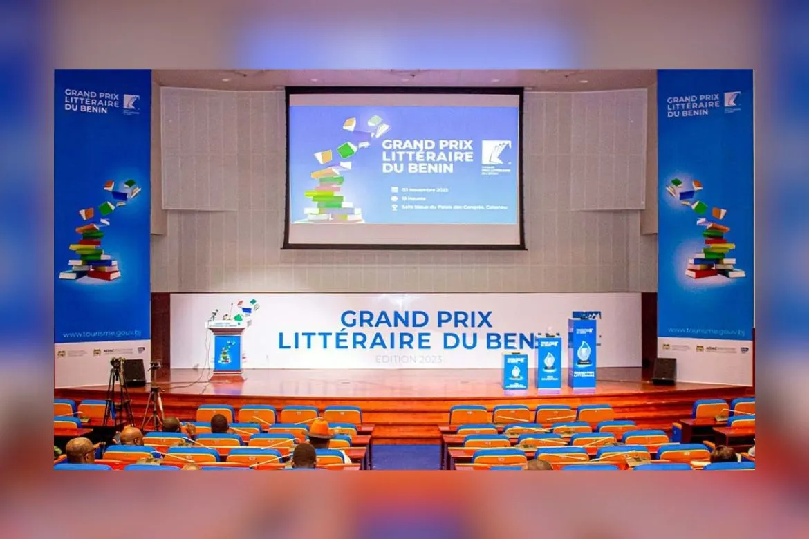 Salle de conférence avec des sièges bleus et une scène ornée de bannières du Grand Prix Littéraire du Bénin
