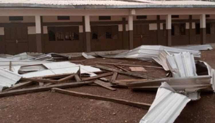 Des tôles métalliques et des débris en bois jonchent le sol devant un bâtiment à plusieurs portes donnant sur un couloir couvert.