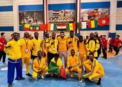 Groupe d’hommes en tenue sportive jaune posant ensemble sur un sol bleu avec plusieurs drapeaux africains en arrière-plan
