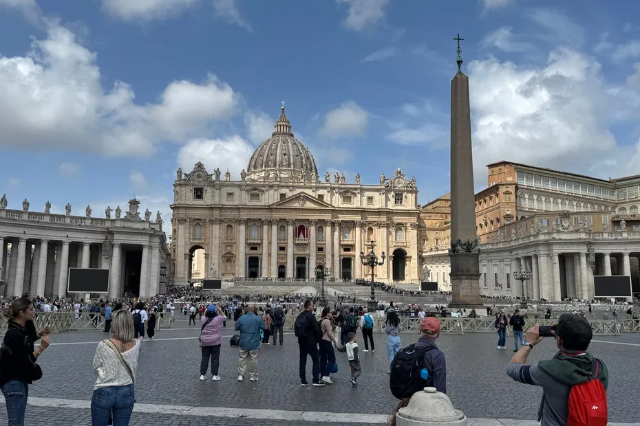 Place animée devant une grande basilique classique sous un ciel bleu ponctué de nuages blancs