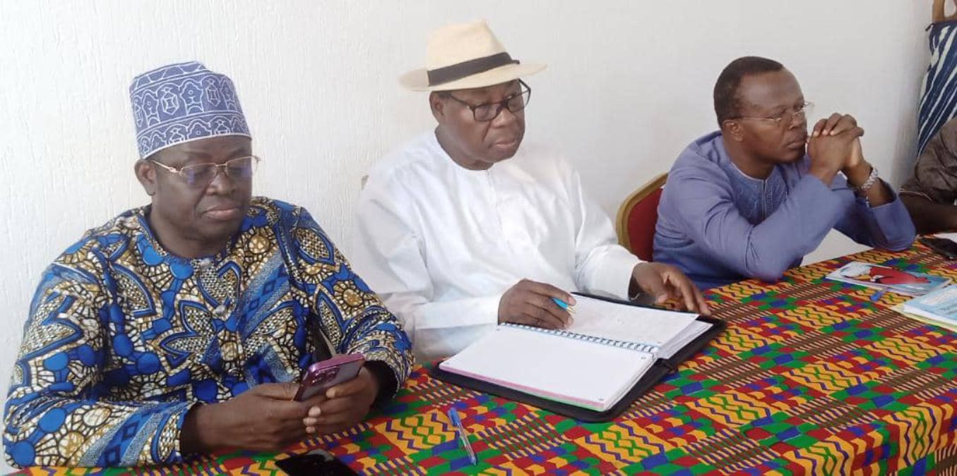Trois hommes assis à une table colorée consultent un carnet et un téléphone portable dans une réunion.