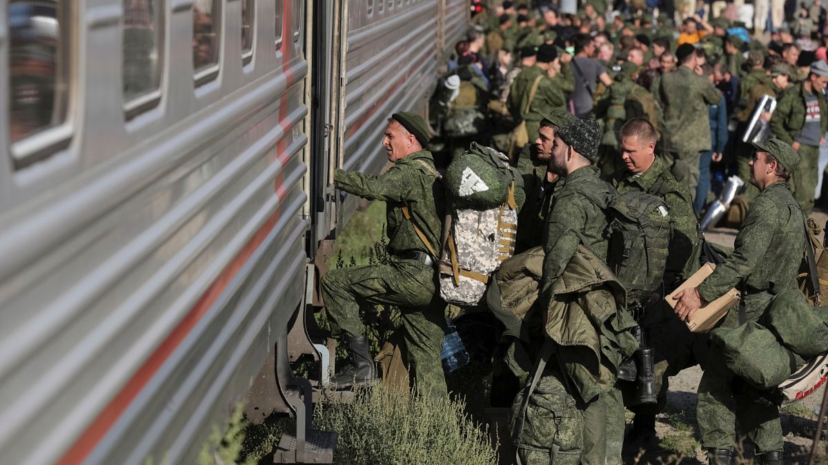 Des soldats en uniforme vert chargent un train militaire sur un quai bondé en plein jour