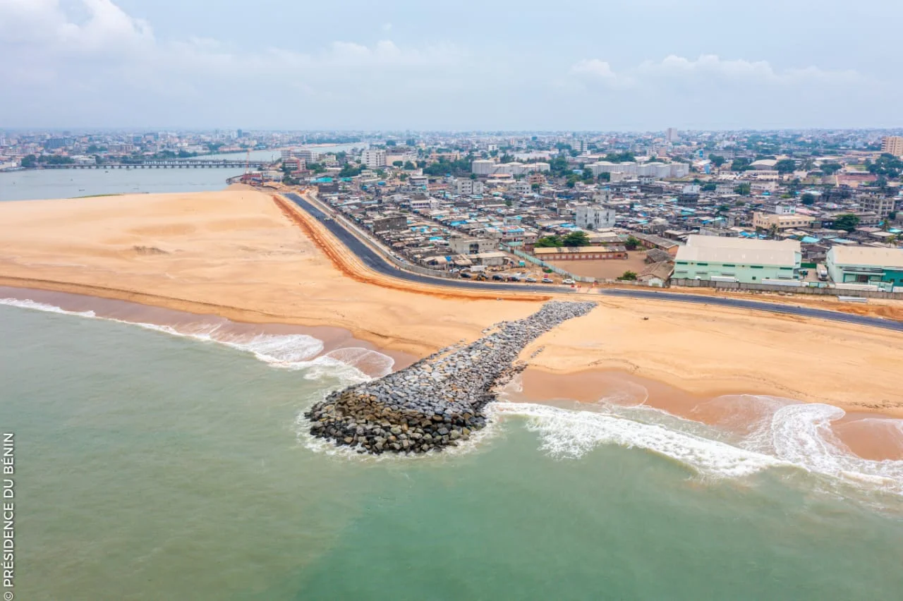 Vue aérienne d’une plage artificielle avec une digue de pierres et une ville dense à l’arrière-plan