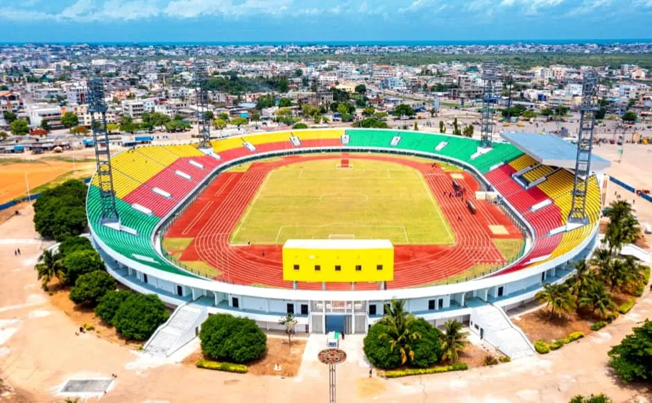 Stade circulaire avec piste d'athlétisme et pelouse au centre entouré de gradins aux couleurs vert, jaune et rouge
