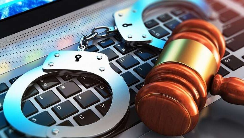 Menottes posées sur un clavier d’ordinateur à côté d’un marteau de juge symbolisant la justice