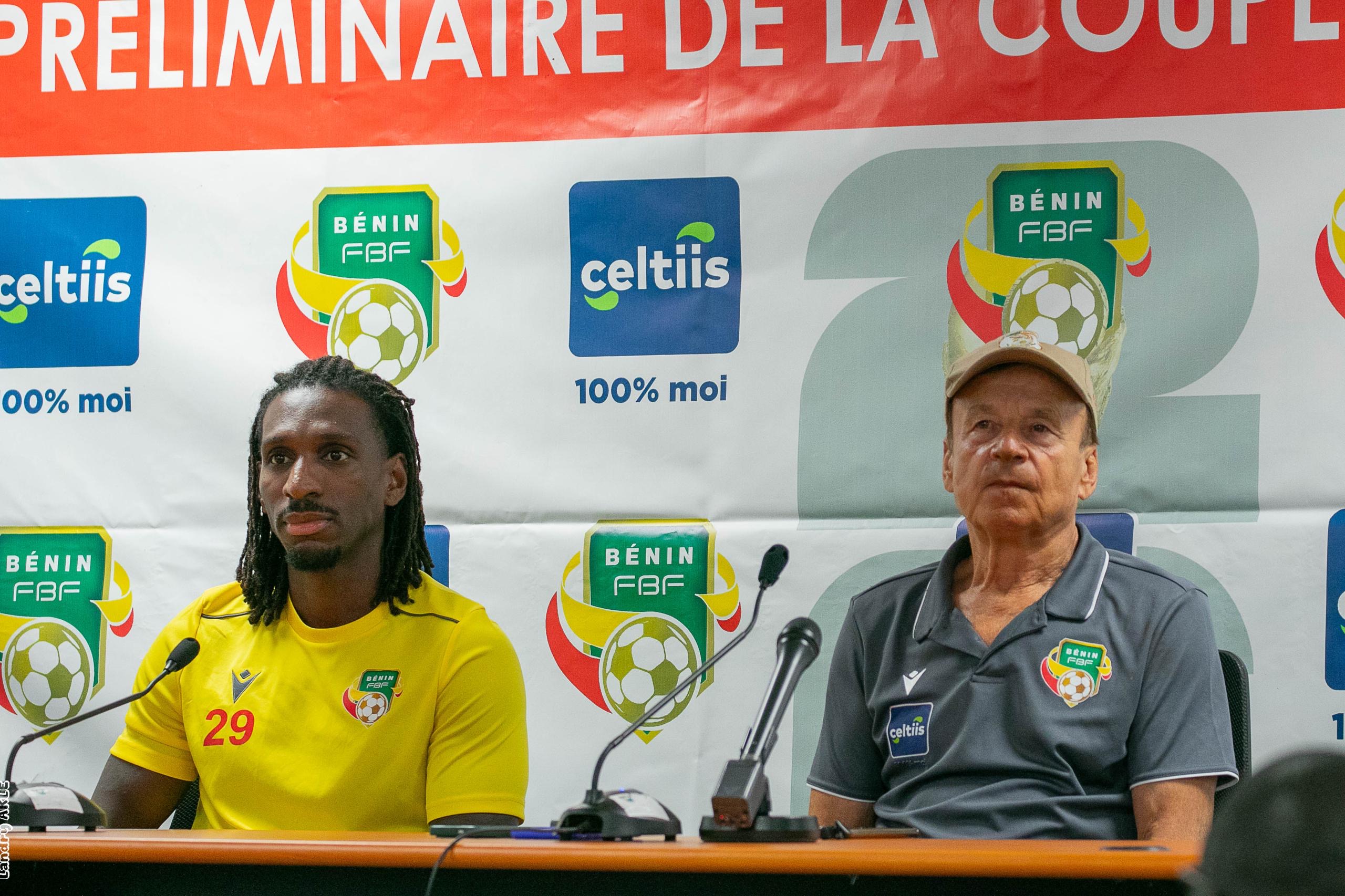 Deux hommes assis derrière une table avec micros devant une affiche d’un événement sportif liée au football au Bénin