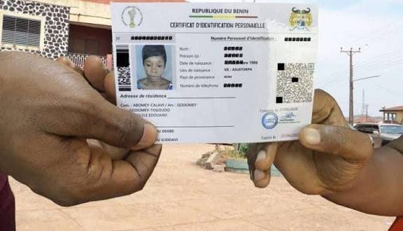 Deux mains tiennent un certificat d'identification personnelle devant une rue avec quelques bâtiments en arrière-plan