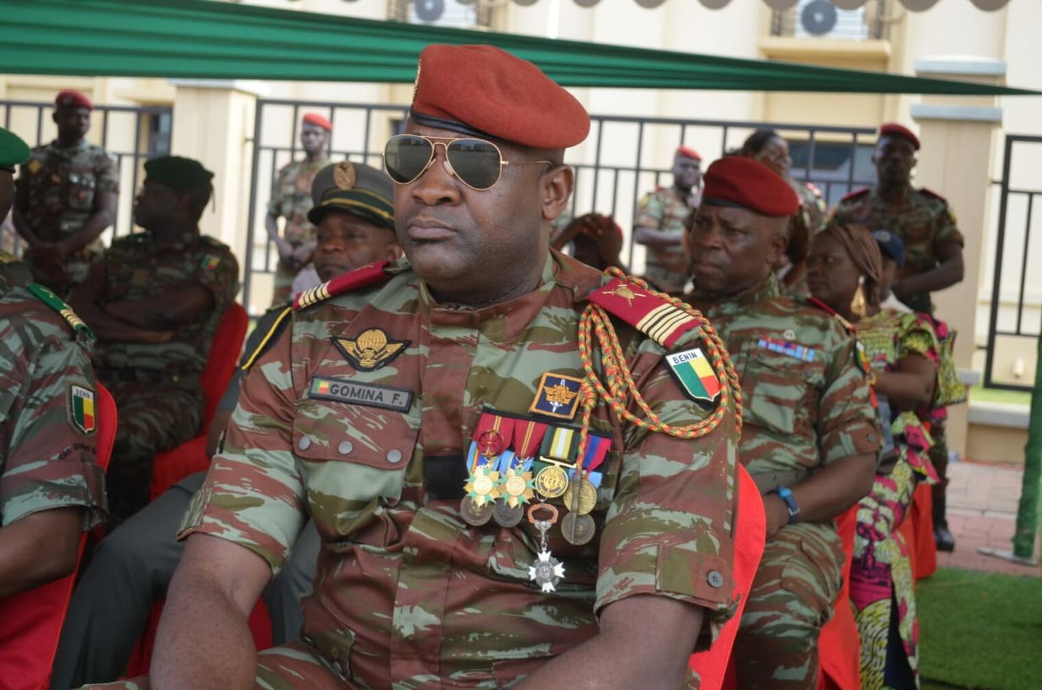 Militaires en tenue de camouflage assis lors d’une cérémonie en plein air sous un abri vert