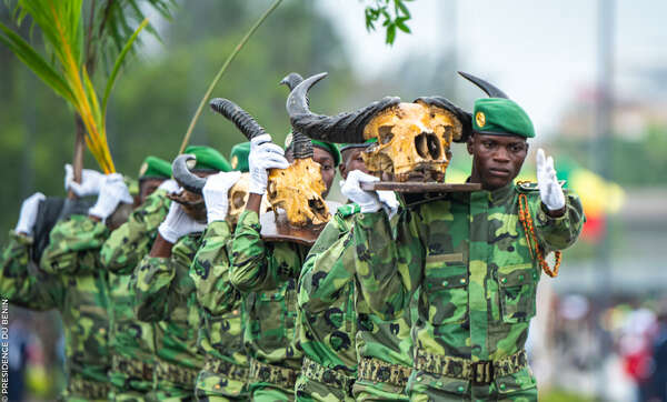 Des militaires en uniforme camouflé et béret vert portent des crânes d'animaux à cornes lors d'une cérémonie en extérieur