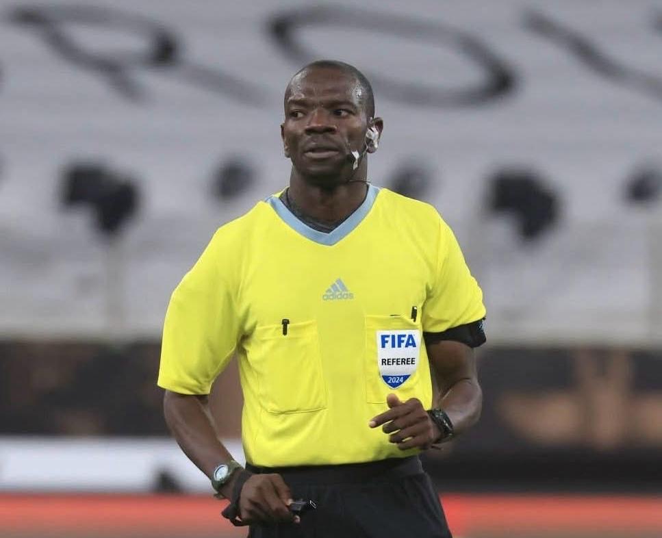 Arbitre en tenue jaune avec badge FIFA en train d'observer le jeu durant un match de football