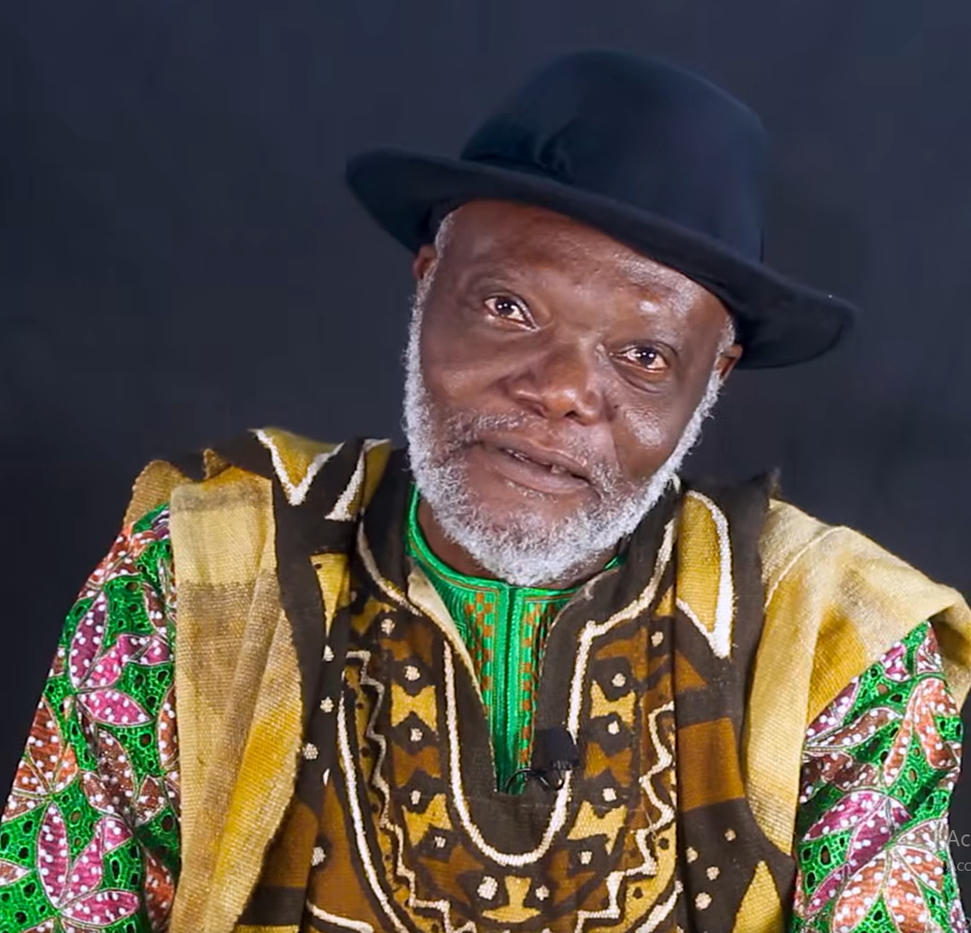 Homme âgé portant un chapeau noir et un vêtement coloré traditionnel africain sur fond sombre