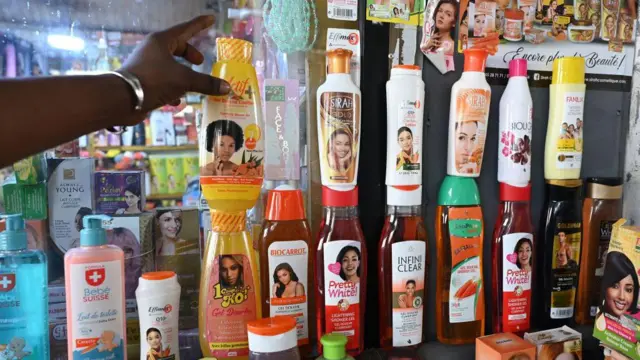 Produits cosmétiques dépigmentants alignés sur un présentoir avec une main tendue vers une bouteille jaune.