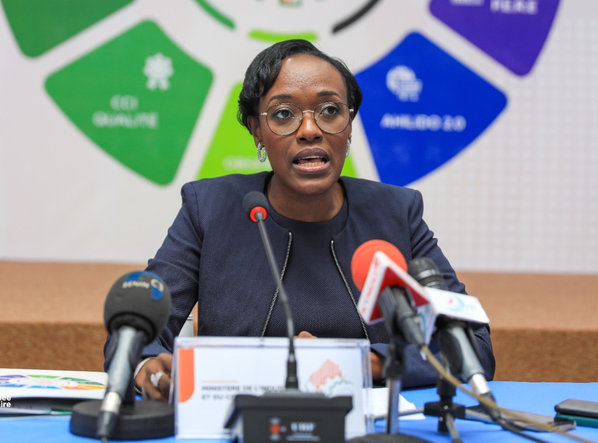 Femme parlant face à plusieurs micros lors d'une conférence avec un logo coloré en arrière-plan