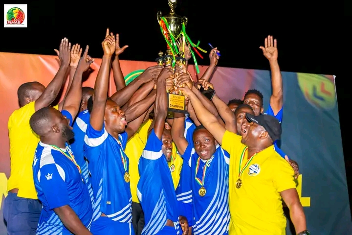 Des joueurs en maillots bleus et un encadrant en jaune lèvent ensemble un trophée de champion sous les acclamations