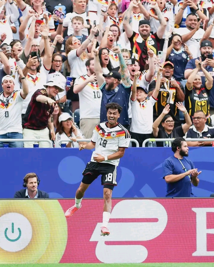 Un joueur en maillot blanc avec le numéro 18 célèbre un but devant des supporters en liesse portant les couleurs allemandes