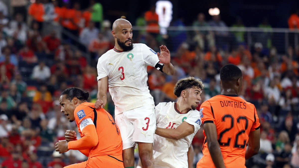 Des joueurs en maillots blancs et orange se disputent un ballon de football en plein match devant un public nombreux