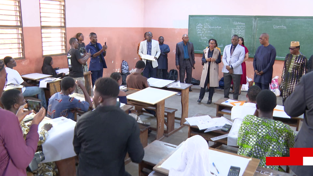 Des enseignants debout devant des élèves assis dans une salle de classe avec des tableaux noirs et des documents sur des bureaux