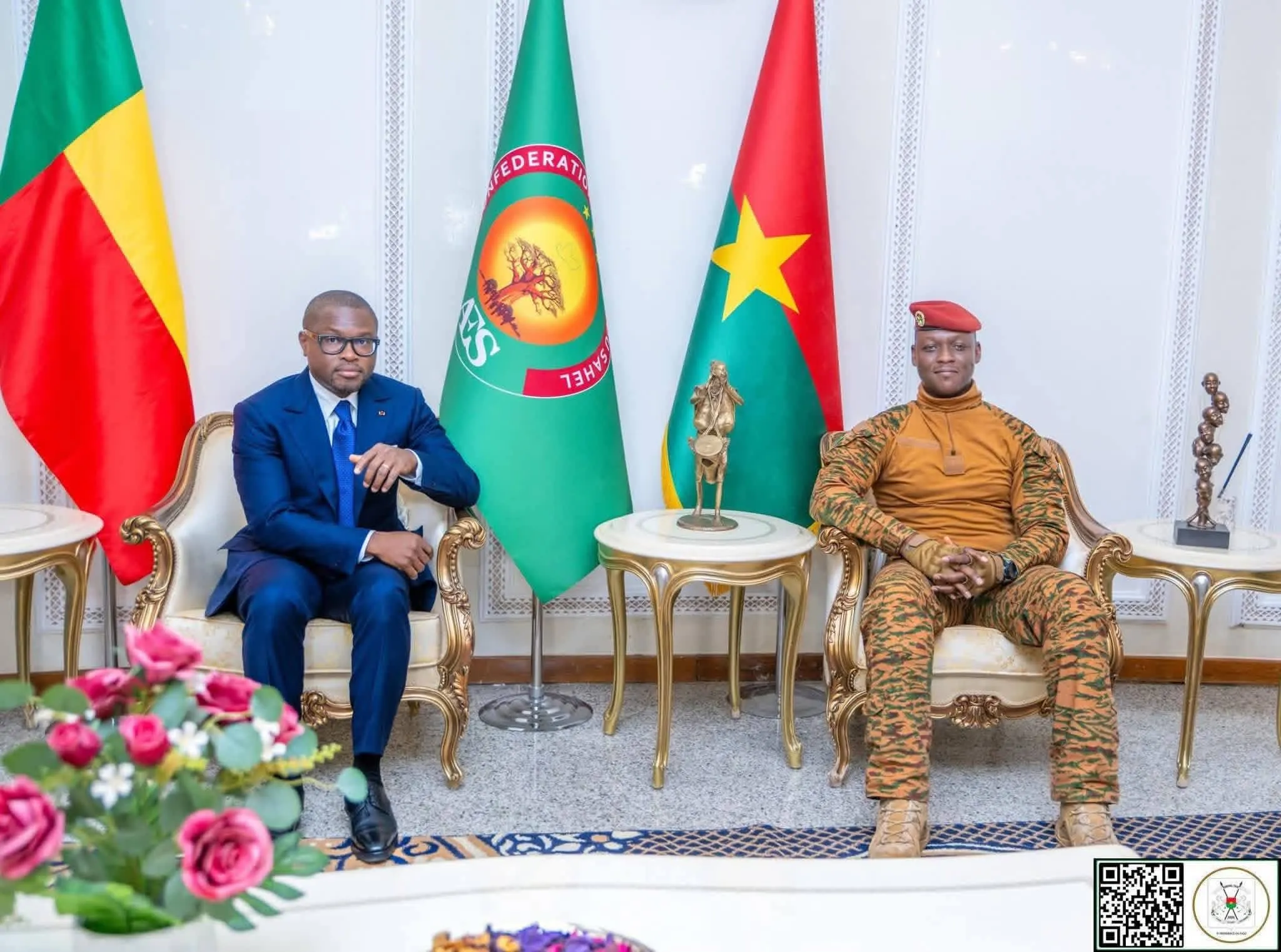 Deux hommes assis sur des fauteuils dorés séparés par une petite table avec drapeaux colorés en arrière-plan