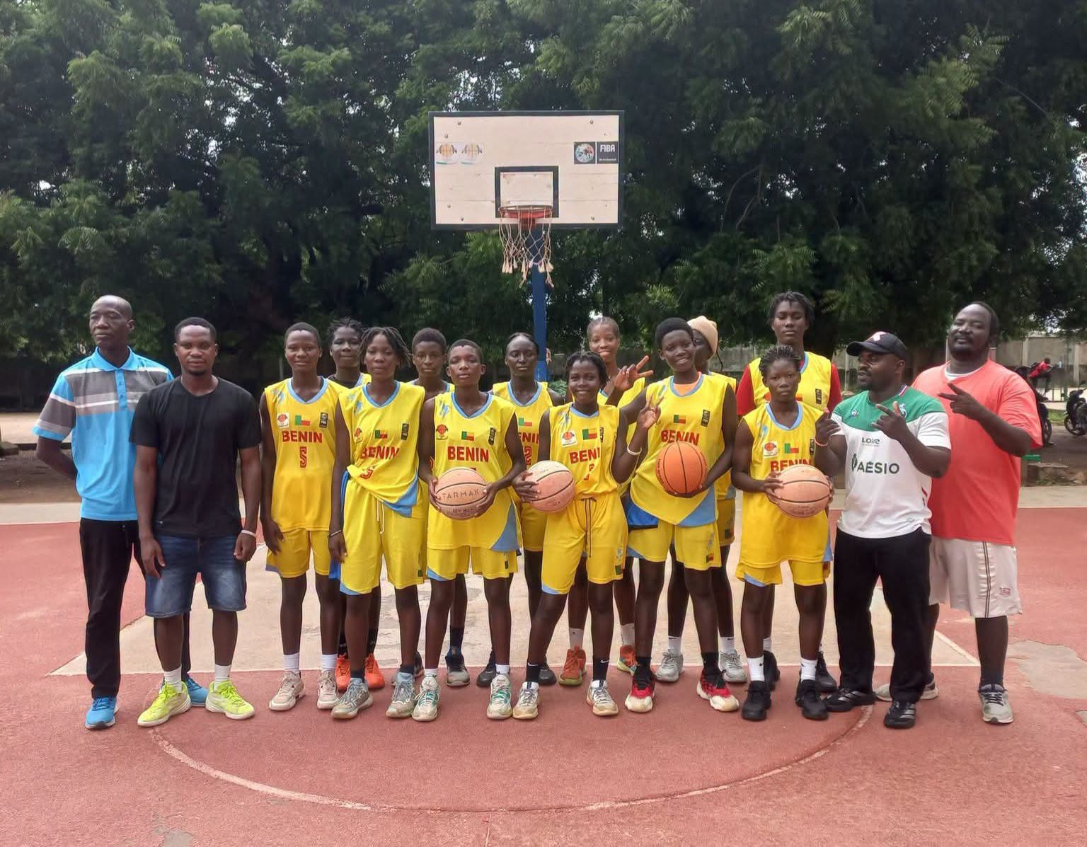 Équipe féminine de basketball en tenue jaune posant sur un terrain extérieur devant un panier avec quatre entraîneurs autour